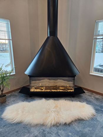 A black wood stove in a room with a white furry rug in front of it.